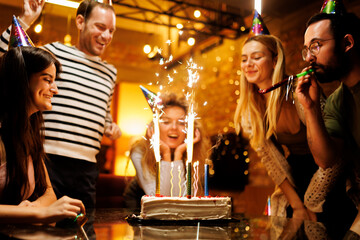 Group of friends celebrating a birthday with a festive cake and sparklers