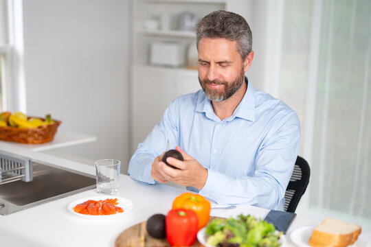 Man eats breakfast in the kitchen on a morning. Middle aged man enjoys fresh food at the kitchen table. A man eats cereal and fruit in the kitchen. Guy enjoys eggs and vegetables at the cozy kitchen.