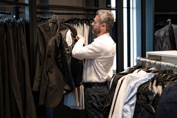 Naklejka premium Business man in a suit in a suit boutique. A businessman confidently chooses elegant suit in store. A trendy customer examines jacket while shopping formal suit. A charming model in classic outfit.