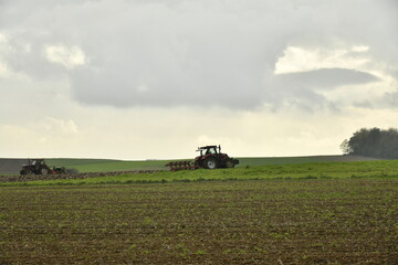 Obraz premium Tracteur labourant un champ sous les gros nuages gris en automne à Ghislenghien (Ath)