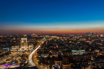 Fototapeta premium The city skyline glows during twilight, showcasing bright buildings and busy streets. Lights twinkle across the horizon as the day transitions to night in this vibrant urban landscape.