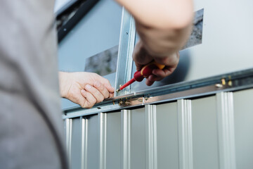 A man uses a screwdriver to attach a roof part while installing a metal shed.