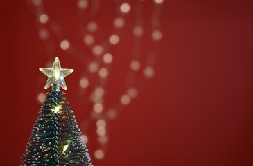 Charming decorative Christmas tree and glowing garland on red background. Happy New Year and Merry Christmas concept. Close up