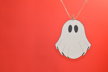 An adorable paper ghost is attached to a string with a clothespin on a red background