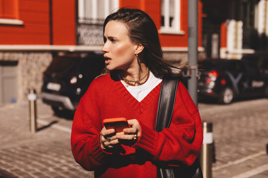 Mad and shock beautiful woman using mobile phone standing in city street. Unhappy woman hold mobile phone. Disappointed sad upset lady horrified impressed news. WTF. Oh no. Woman wear red sweater.