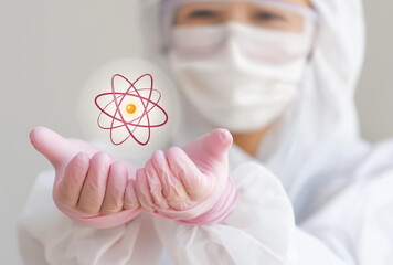  a woman in a white protective suit and pink gloves holds an atomic model with the symbol of radiation