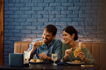 Happy couple enjoying in sandwiches while eating in restaurant.