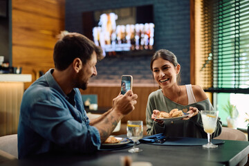 Happy couple having fun and taking picture while eating in restaurant.