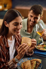 Happy woman eating sandwich on lunch date in restaurant.