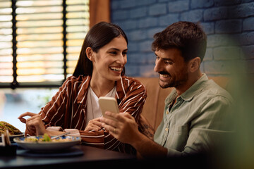 Happy couple talking while using cell phone in restaurant.