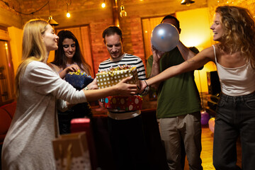 Friends gathering at a cozy indoor evening celebration with gifts and balloons, creating happiness and shared laughter as they enjoy a festive and heartfelt moment together.