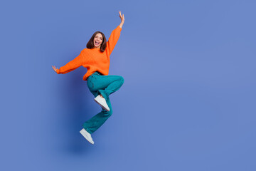 Obraz premium Excited young woman in orange sweater jumps joyfully against a purple-blue background wearing casual trendy outfits