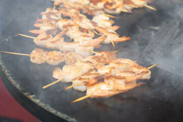 Seafood skewers grilling over hot flames at a vibrant outdoor festival in a lively urban location during summer, showcasing the enticing aroma of fresh shrimp