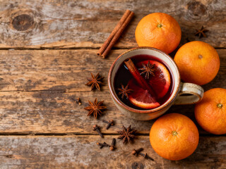 A cozy spiced drink sits in a mug, adorned with cinnamon and orange slices. Fresh oranges and star anise surround the cup. Copy space