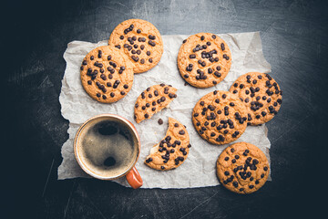 Homemade Chocolate chip cookies with coffee on paper over dark background, top view