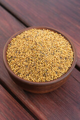Mustard seeds in rustic clay bowl on wooden table