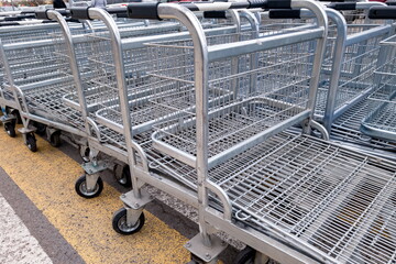 Metal shopping carts are lined up neatly in a supermarket parking area during a sunny day, ready for shoppers to use
