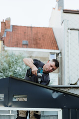 Mature handyman installing roofing sheets with drill on metal shed.