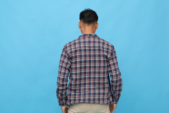 Rear view of young Asian man standing isolated on blue background.