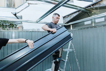 A mature man prepares to install roofing sheets on a metal shed.