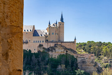 Fototapeta premium The Alcázar of Segovia, Spain (c. 1120): This majestic royal fortress with distinctive slate spires stands on a rocky crag against a clear blue sky, a Spanish medieval landmark