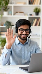 Smiling young man with headset waving during video call while working remotely from home with laptop.