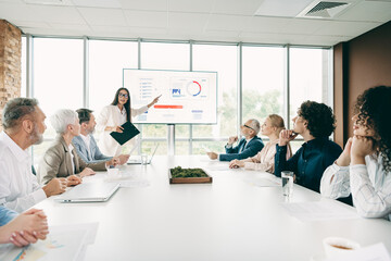 Business team meeting in a modern office with diverse members deliberating strategy and analyzing charts displayed on screen.