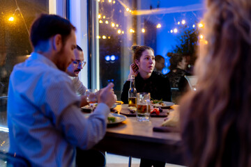 Friends enjoying a dinner gathering in a warm, festive atmosphere with conversations and good food under cozy lighting at a restaurant.