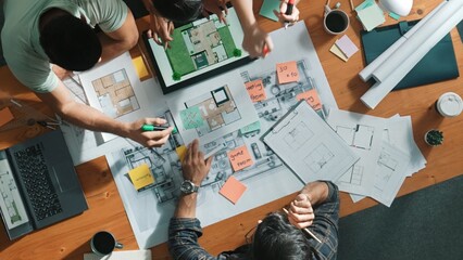 Top down view of manager writing at blueprint while marketing team plans design. Aerial view of architect engineer working together sharing idea and taking a note in project plan at table. Symposium.