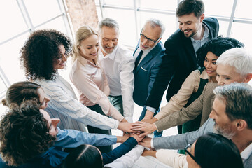 Diverse office team collaborating with hands together during business meeting, symbolizing unity,...