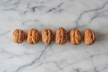 Close-up of walnuts in their shells lined up on white marble