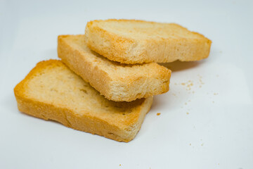 Three golden-brown Indian rusks are neatly stacked on a clean white background in a studio setting. This close-up highlights their crunchy texture and warmth.
