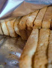 Close-up of golden toasted rusk slices neatly arranged inside a shiny metallic pouch in India, with crumbs visible at the bottom.