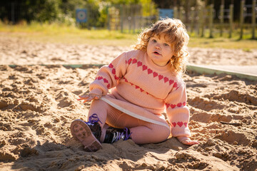 Child playing in sandy area wearing warm sweater on a bright sunny day outdoors