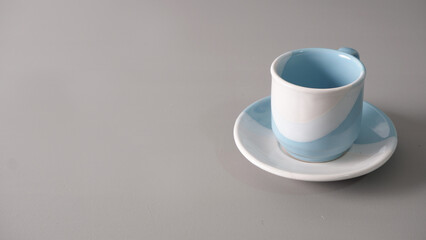 A small, two-toned blue and white ceramic coffee cup rests on a matching saucer against a plain gray background.