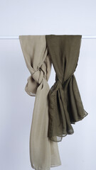 Two textured scarves, one beige and one olive green, are draped and knotted against a plain white background.