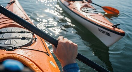 Obraz premium Close-up of kayaker's hand on paddle with orange kayaks in sparkling water