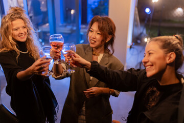 Group of joyful friends celebrating with glasses of wine during an evening gathering at a cozy and illuminated indoor setting