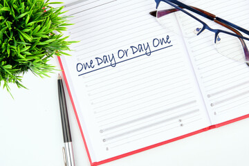 An open day planner displays One Day Or Day One at the top of the page Glasses rest nearby, with a...