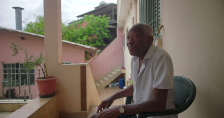 African American Elderly man sitting on porch smiling, showing wisdom and warmth, with a contemplative expression, surrounded by tropical residential background