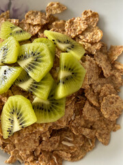 A close-up image showing a bowl of breakfast bran flakes topped with freshly sliced kiwi fruit.