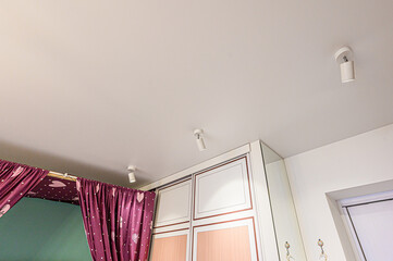 Bright interior with a white ceiling, track lighting, a wardrobe, and pink heart-patterned curtains