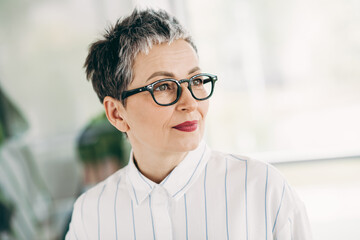 Professional middle-aged businesswoman wearing glasses sitting in a modern office environment...