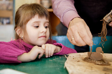 A preschool girl is engaged in clay modeling in a ceramics class. Every Saturday, the children are eager to go to their ceramics class and create pottery.