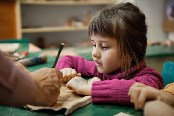 A preschool girl is engaged in clay modeling in a ceramics class. Every Saturday, the children are eager to go to their ceramics class and create pottery.