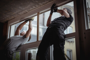 Two guys work together to seal cracks with tape on a window frame.