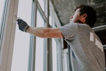 A male builder repairs a plastic window in a house.