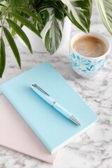 Blue haze stationery flat lay featuring a notebook, pen, and coffee cup on a marble surface with a plant, creating a serene workspace atmosphere for creative inspiration