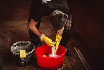 A worker washes a plastic part of a frame in a bucket with soap.