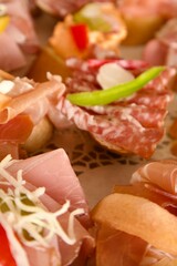 Assorted canapés with ham, salami, cheese, and vegetables, garnished with herbs and pepper, served on a festive table for a wedding celebration.